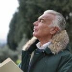 An older man reading a book in a park, seeking diet advice.