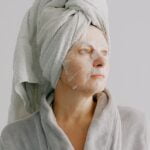 A woman in a robe with a face mask on, providing anti-aging tips.