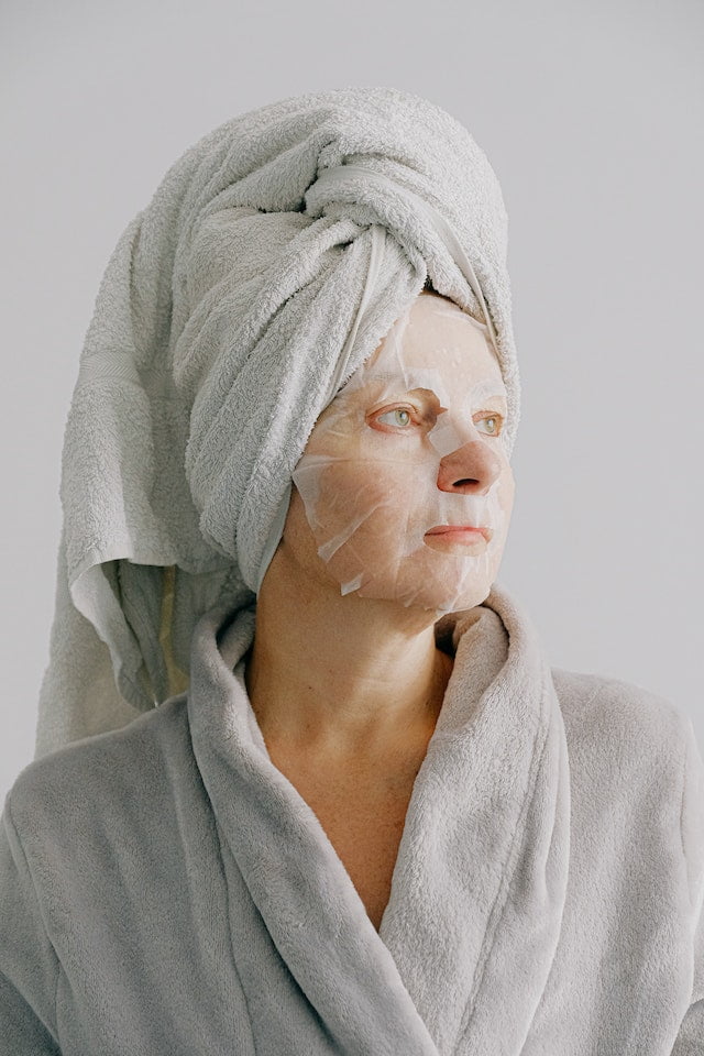 A woman in a robe with a face mask on, providing anti-aging tips.