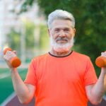 A man with a beard is holding two orange dumbbells while sharing anti-aging tips.