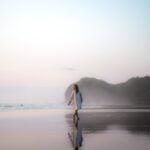 A woman enjoying a peaceful sunset walk on the beach, finding solace and tranquility amidst the beauty of nature.