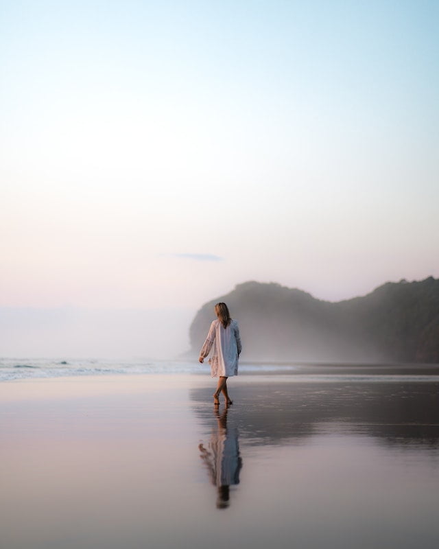 A woman enjoying a peaceful sunset walk on the beach, finding solace and tranquility amidst the beauty of nature.