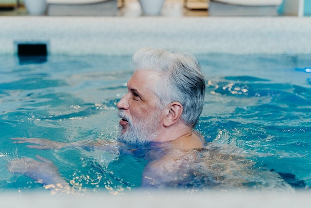 A man in a swimming pool, showcasing his wellness and longevity tips lifestyle while maintaining a white beard.