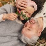 An older couple demonstrate anti-aging tips by laying on the ground with a flower in their mouth.