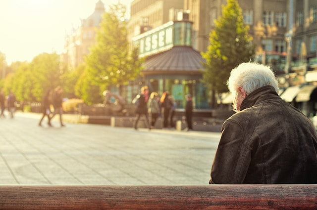 An older man sitting on a bench in a city, showcasing senior health and longevity tips.