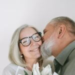 An older couple kissing while holding a bouquet of tulips demonstrating longevity and wellness in their relationship.