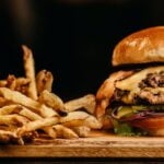 Aging tips for a burger and fries on a wooden cutting board.