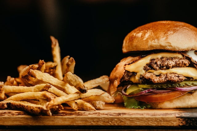 Aging tips for a burger and fries on a wooden cutting board.