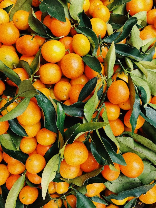 A pile of tangerines with green leaves, offering diet advice for wellness tips.