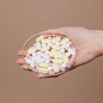 A woman's hand holding a plate of pills on a brown background, offering wellness tips for longevity.