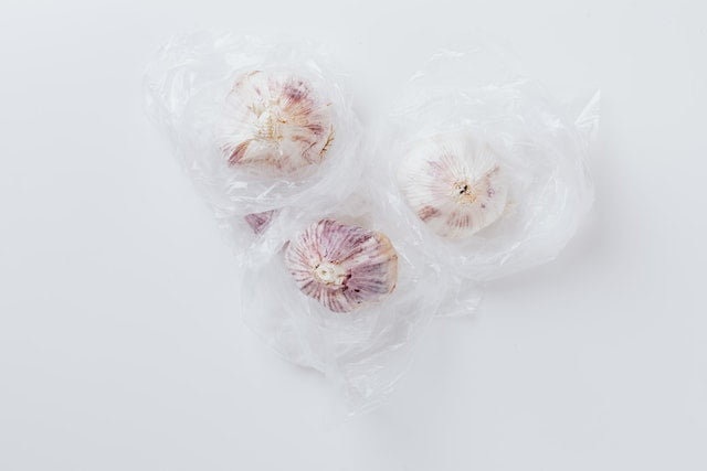Three garlic cloves in plastic bags on a white background, offering anti-aging tips and diet advice.