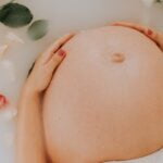 A pregnant woman is peacefully laying in a bathtub with flowers, promoting wellness and relaxation.