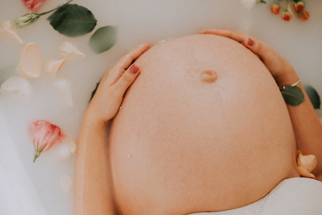 A pregnant woman is peacefully laying in a bathtub with flowers, promoting wellness and relaxation.