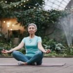 A woman is meditating in a greenhouse, seeking wellness tips for longevity.