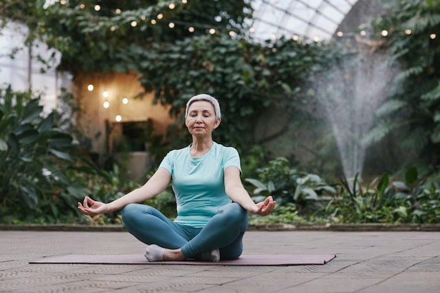 A woman is meditating in a greenhouse, seeking wellness tips for longevity.