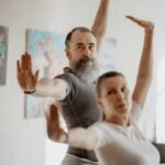 A man and woman practicing yoga for wellness in a living room.