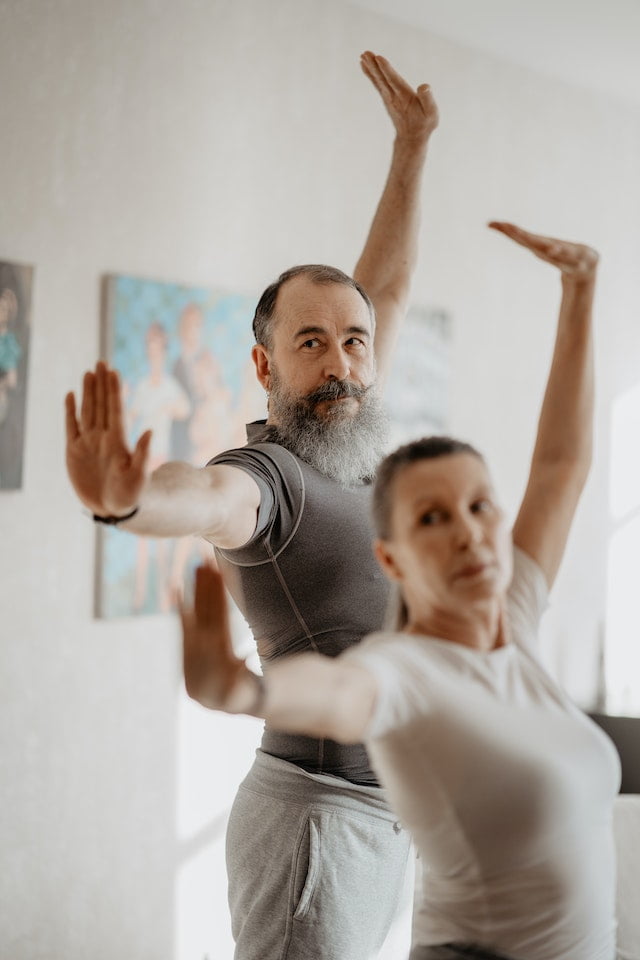 A man and woman practicing yoga for wellness in a living room.