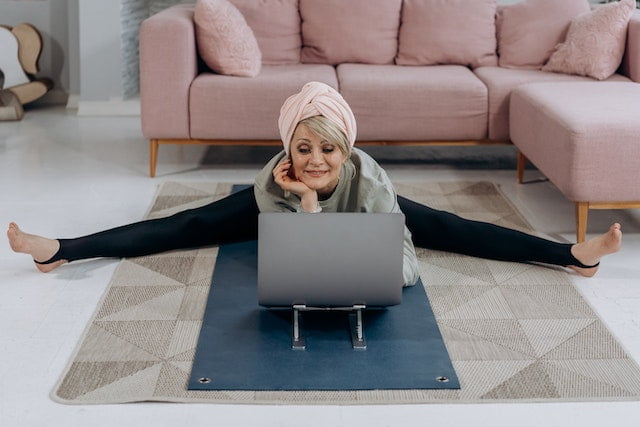 A woman sitting on a yoga mat and using a laptop, seeking wellness tips for senior health.