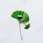 A ginkgo leaf and a pill on a marble table, providing wellness and anti-aging tips.