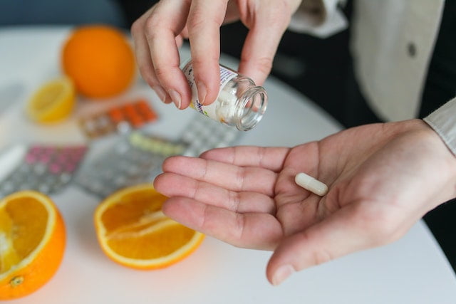 A woman is putting pills into a bottle next to oranges, following wellness tips.