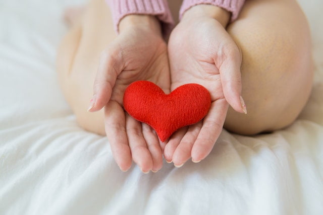 A woman's hands holding a red heart on a bed, promoting wellness tips.