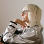 An older woman wearing glasses and a silver jacket, sharing wellness tips for senior health.