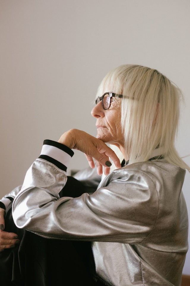 An older woman wearing glasses and a silver jacket, sharing wellness tips for senior health.