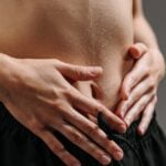 A woman is holding her stomach with her hands, seeking wellness tips for her discomfort.