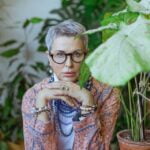 A woman in glasses sits in front of a potted plant, providing diet advice for senior health.