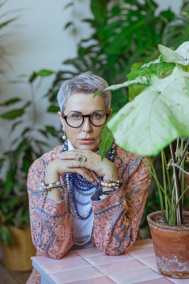 A woman in glasses sits in front of a potted plant, providing diet advice for senior health.