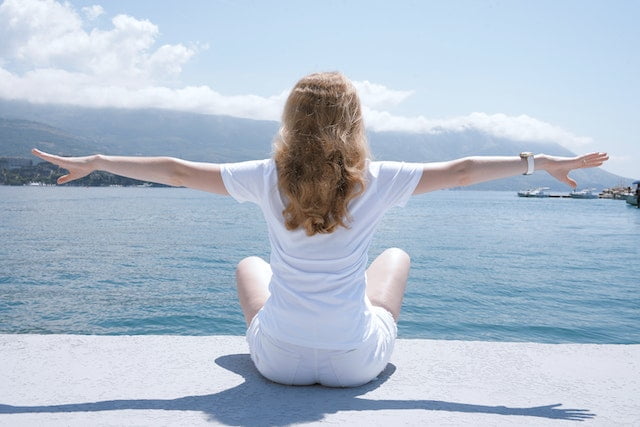 A woman with her arms outstretched by the water, radiating serenity and embracing the blissful benefits of longevity.