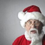 A man in a santa claus costume makes a surprised face while sharing wellness tips.