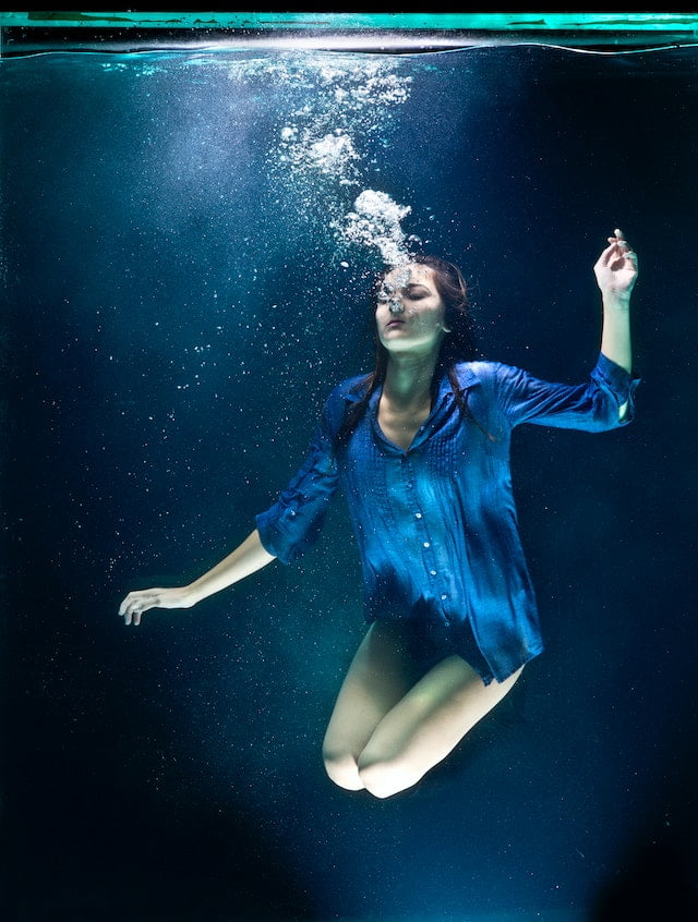 A woman is swimming underwater in a blue shirt, showcasing her senior health and wellness.
