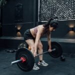 A woman lifting a barbell in a gym, seeking aging tips and longevity tips.