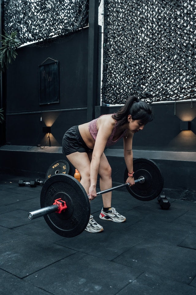 A woman lifting a barbell in a gym, seeking aging tips and longevity tips.