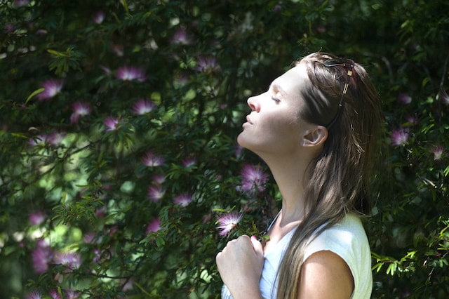 A woman is standing in front of a flowering bush, seeking diet advice for anti-aging tips.