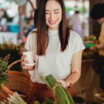 Asian woman holding a cup of coffee at a market, seeking senior health tips.