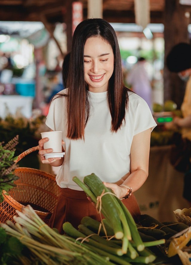 Asian woman holding a cup of coffee at a market, seeking senior health tips.
