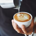 A person pouring latte into a cup of coffee, offering diet advice for senior health.