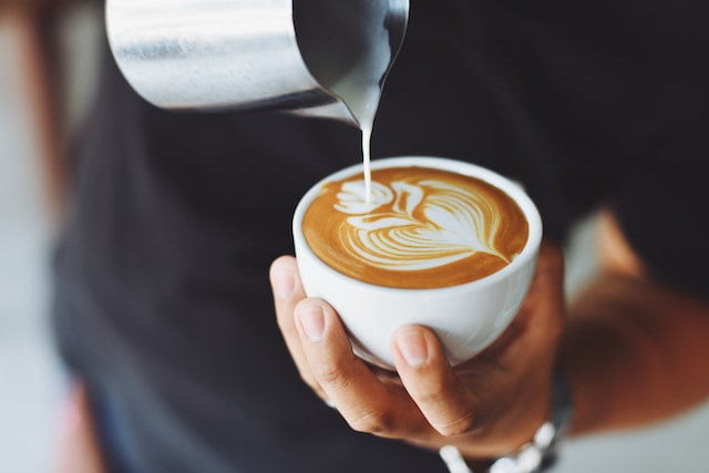 A person pouring latte into a cup of coffee, offering diet advice for senior health.