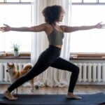 A woman practicing yoga in front of a window with her dog, incorporating wellness tips for senior health.