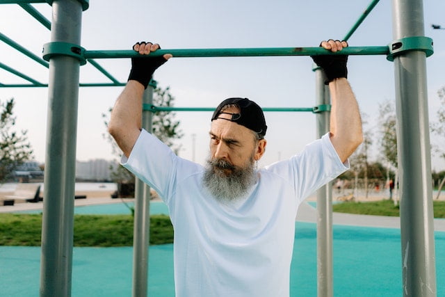 A man with a beard doing pull ups in a park, showcasing his impressive longevity and fitness regime.