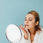 A senior woman is applying makeup in front of a mirror, incorporating wellness tips into her daily routine for improved longevity and overall senior health.