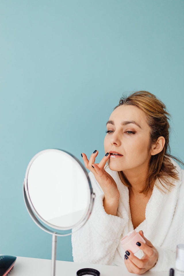 A senior woman is applying makeup in front of a mirror, incorporating wellness tips into her daily routine for improved longevity and overall senior health.