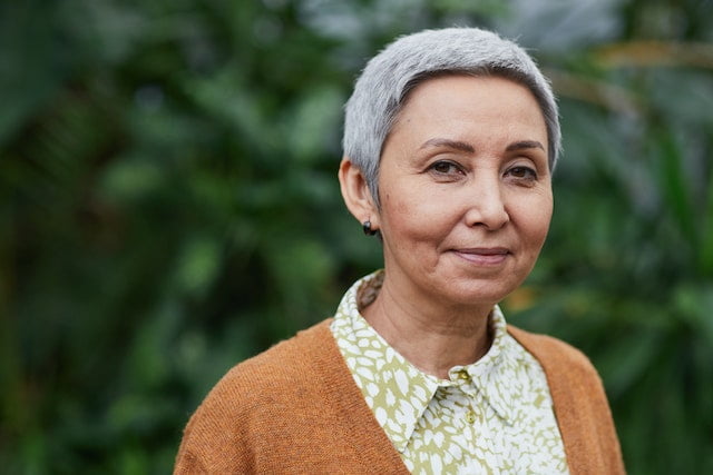 A woman with gray hair standing in front of plants, symbolizing the ideal embodiment of senior health.
