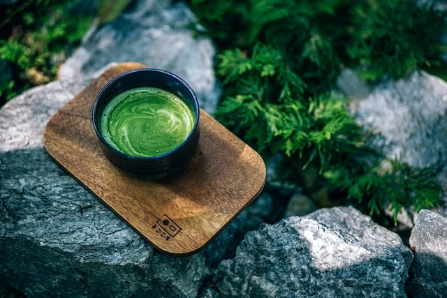 A cup of green tea, known for its wellness benefits, delicately placed on top of rocks.