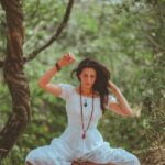 A woman in a white dress sitting on a rock in the woods overlooking a serene lake, radiating timeless beauty and grace.