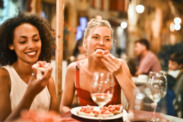 Two senior women enjoying pizza at an outdoor restaurant, while exchanging anti-aging tips.