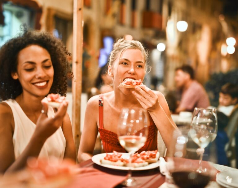 Two senior women enjoying pizza at an outdoor restaurant, while exchanging anti-aging tips.