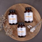 Three jars of supplements filled with wellness tips on a wooden plate.